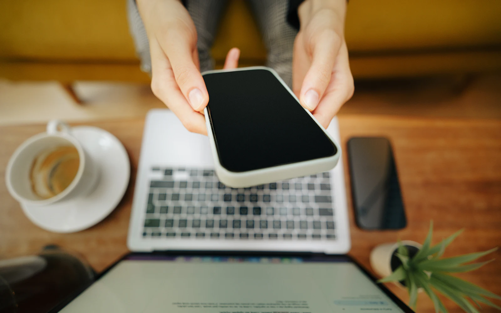 Dłonie trzymające smartfon nad klawiaturą laptopa